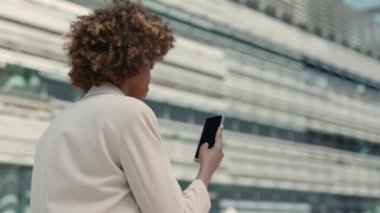 Afro-Amerikalı iş kadını. Şehir caddesinde yürürken internette akıllı telefondan sörf yapıyor. Yaşam tarzları için modern aletler. Başarılı insanlar..