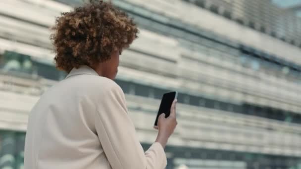 Mujer de negocios afroamericana navegando por Internet en un teléfono inteligente mientras camina por la calle de la ciudad. Aparatos modernos para estilos de vida. Personas exitosas. — Vídeo de stock