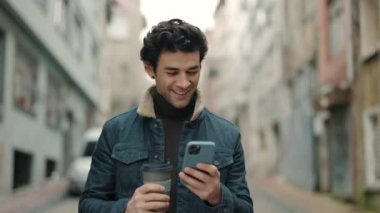 Kahveli ve akıllı telefonlu neşeli adam sokakta yürüyor.