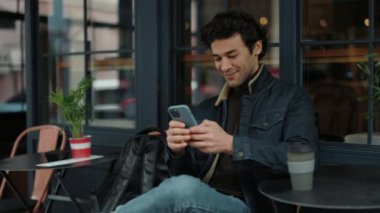 Kafe terasında otururken akıllı telefon kullanan gülümseyen adam.