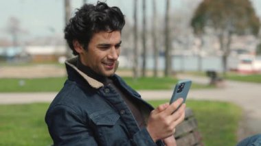 Güzel görünümlü Arap adam bankta oturuyor ve cep telefonu kullanıyor.