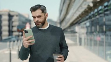Başarılı bir adam kahve ve cep telefonuyla sokakta yürüyor.