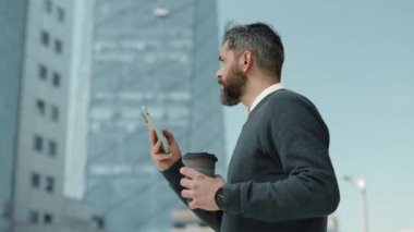 İş adamı kahve tutuyor ve dışarıda cep telefonu kullanıyor.