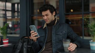 Kafe terasında oturan ve akıllı telefon kullanan mutlu adam.