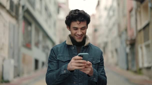 Knappe vent die op straat loopt en een mobieltje gebruikt — Stockvideo