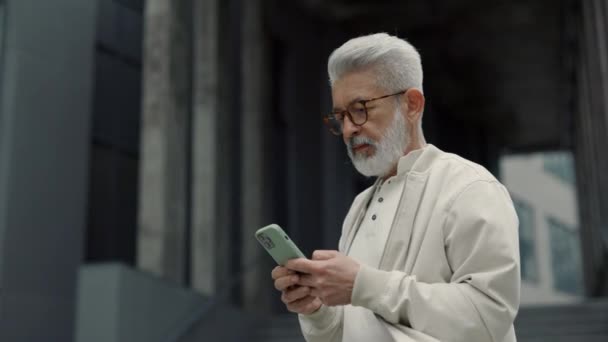 Homme âgé debout à l'extérieur et travaillant sur mobile — Video