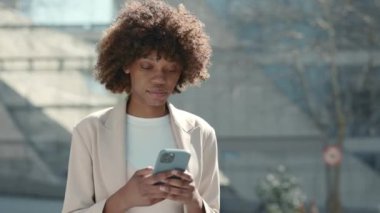 Ciddi bir Amerikalı kadın açık havada yürüyor ve cep telefonu kullanıyor.