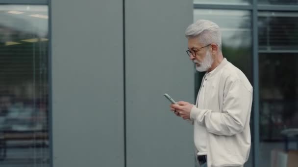 Hombre mayor que tiene chat en línea en el teléfono inteligente al aire libre — Vídeo de stock
