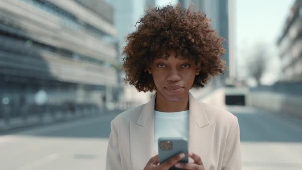 Portré mosolygós afrikai hölgy formális ruha segítségével mobil az utcán — Stock videók