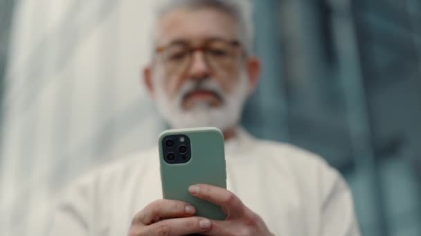 Ηλικιωμένος άνδρας που στέκεται στο δρόμο και πληκτρολογεί μηνύματα στο κινητό — Αρχείο Βίντεο