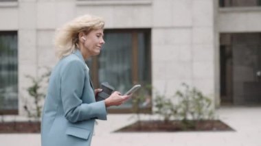 Dışarıda yürürken cep telefonu kullanan ve kahve içen bir kadın.