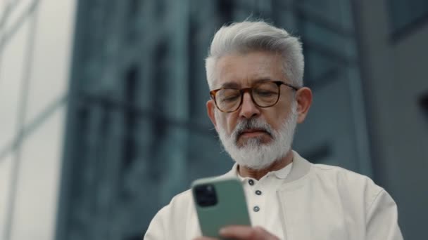 Σοβαρός ηλικιωμένος άνδρας που στέκεται έξω και χρησιμοποιεί κινητό τηλέφωνο — Αρχείο Βίντεο