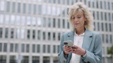 Akıllı telefon kullanan ve dışarıda gülümseyen bir iş kadını.