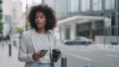 Kahve ve cep telefonuyla yürüyen şık bir iş kadını.