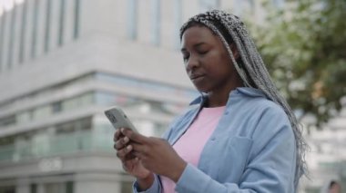 Afro-Amerikalı kadın şehir caddesinde akıllı telefon kullanıyor.