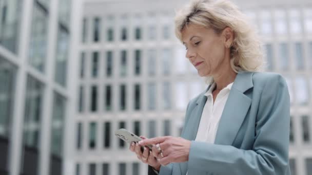 Olgun iş kadını dışarıda akıllı telefondan mesaj atıyor. — Stok video