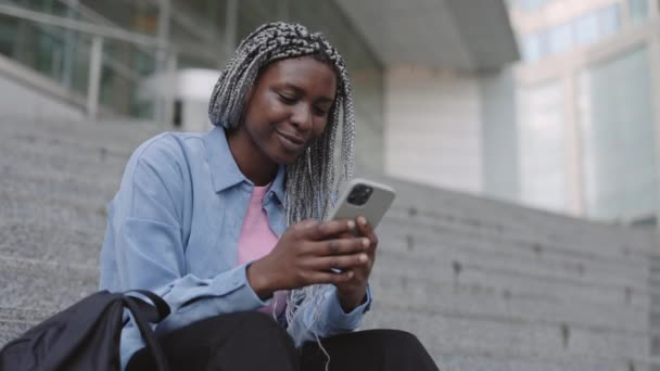 Позитивна жінка смс на мобільний, сидячи на відкритому повітрі — стокове відео