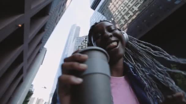 ヘッドフォンの女性は手にコーヒーと路上で踊る — ストック動画