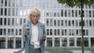 İş kadını kulaklık takıyor, cep telefonu kullanıyor ve kahve içiyor.