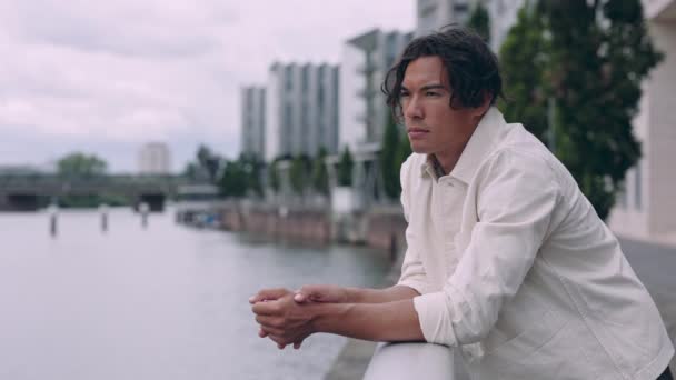 Asijské muž v ležérní oblečení stojící v blízkosti města řeky — Stock video