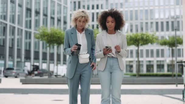 Kahve ve cep telefonuyla sokaklarda yürüyen iş kadınları. — Stok video