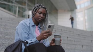 Afrika kökenli Amerikalı kadın kahve içiyor ve cep telefonu kullanıyor.