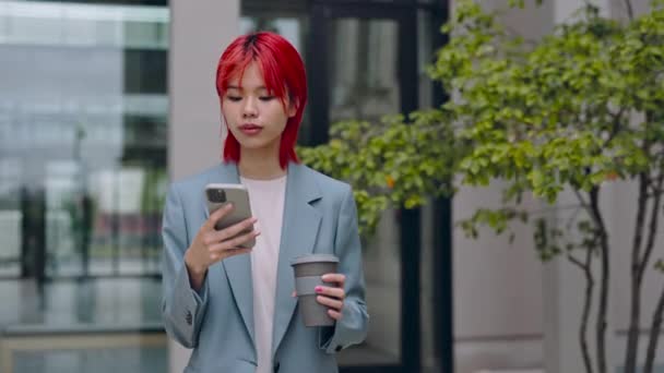 Mujer asiática usando móvil y llevando café en la calle — Vídeos de Stock