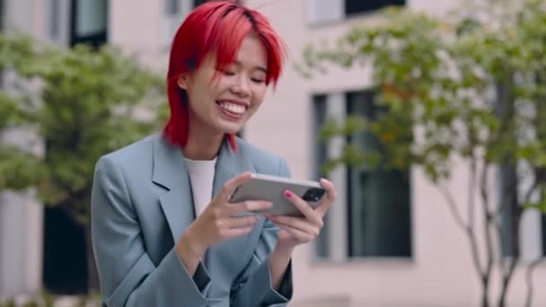 Азійка дивиться на мобільний з зубатою посмішкою на обличчі. — стокове відео