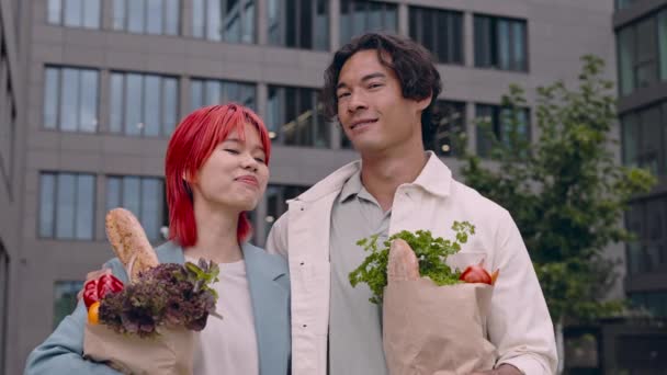 Egy boldog pár pózol az utcán, táskákkal a kezükben. — Stock videók