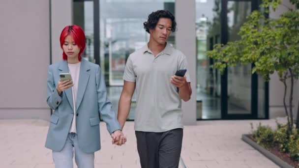 Couple holding hands and using smartphones on street — Stock Video