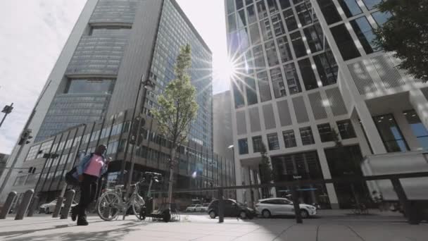 Frankfurt, Alemania, agosto de 2021: Vista de bajo ángulo de una mujer afroamericana con mochila caminando por la calle y usando un teléfono inteligente. La vida de la gran ciudad y el concepto de artilugios modernos. — Vídeos de Stock