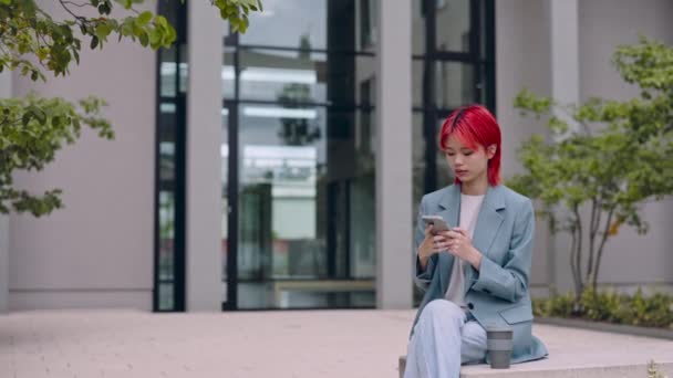 Asian woman sitting outdoors and texting on smartphone — Stock Video