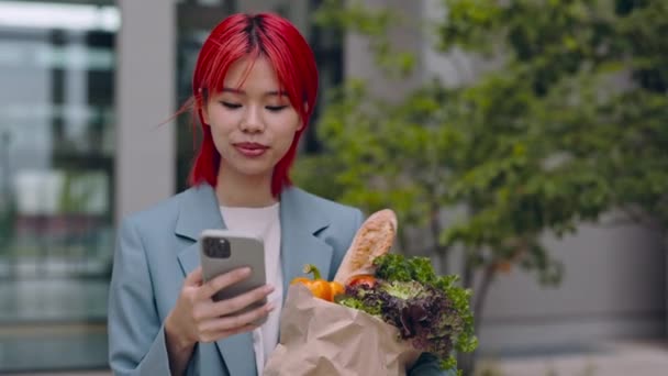 Mujer asiática llevando bolsa de comestibles y el uso de teléfono inteligente — Vídeos de Stock