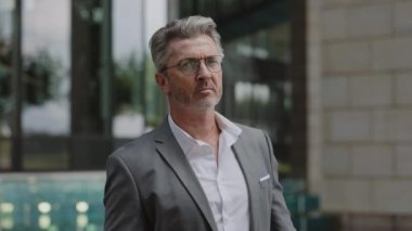 Şehir caddesinde poz veren çapraz kollu olgun iş adamı.