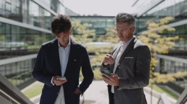 Açık havada akıllı telefon kullanan iki takım elbiseli ortak.