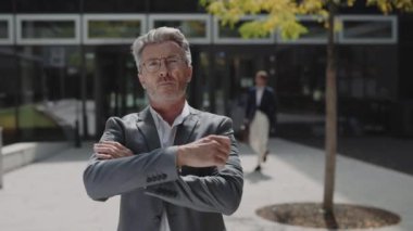 Yaşlı işadamı dışarıda kollarını kavuşturmuş poz veriyor.