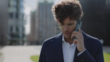 İş adamı dışarıda yürürken cep telefonuyla konuşuyor.