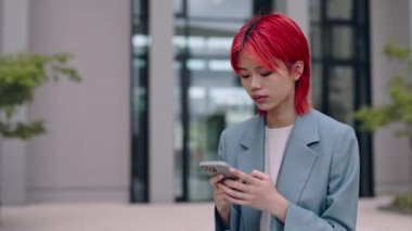 Asyalı kadın sokakta dikiliyor ve akıllı telefon kullanıyor.