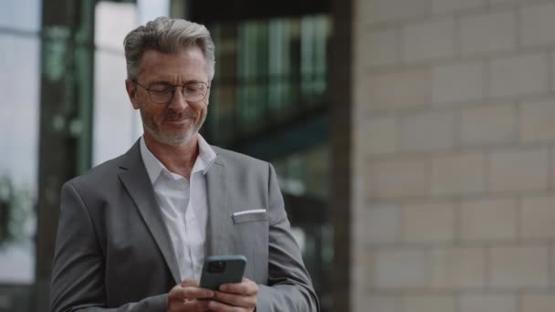 Obchodník v brýlích stojící na ulici a pomocí mobilních — Stock video