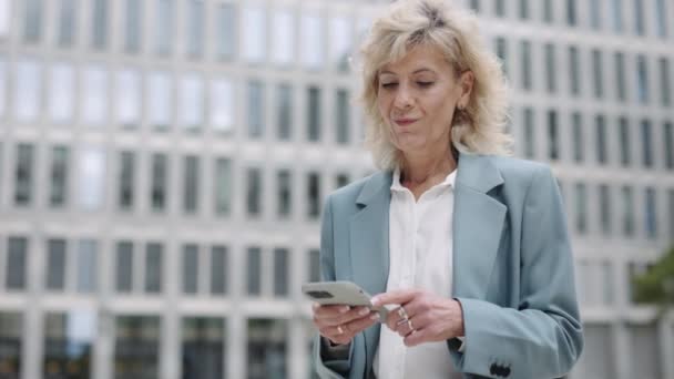 परिपक्व व्यवसायी महिला मोबाइल पर अच्छी खबर पढ़ रही — स्टॉक वीडियो