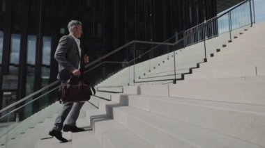Takım elbiseli yaşlı bir adam elinde bavulla merdivenlerden çıkıyor.