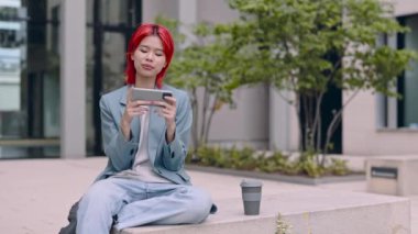 Açık havada akıllı telefon kullanan gülümseyen Asyalı kadın.