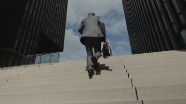 Takım elbiseli yaşlı bir adamın merdivenlerden çıkışının arkası.