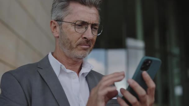 Зрелый мужчина в очках и костюме с помощью мобильного на открытом воздухе — стоковое видео