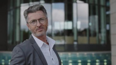 Resmi kıyafetli yaşlı bir adam ofis merkezinin yanında duruyor.