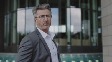 Takım elbiseli ve gözlüklü adam dışarıda poz veriyor.