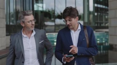 İş arkadaşları konuşuyor ve ellerinde cep telefonuyla yürüyor.