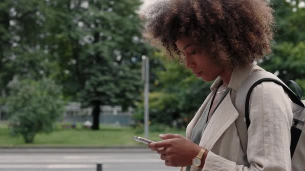 Kobieta z plecakiem stojąca na ulicy i korzystająca z telefonu komórkowego — Wideo stockowe