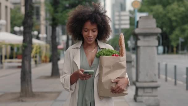 Woman using mobile walking on street with grocery bag — Stock Video