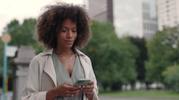 Donna d'affari afroamericana in elegante usura camminare per strada e gesticolare dalla felicità durante la lettura di buone notizie su smartphone moderno. Concetto di persone, successo e tecnologia. — Video Stock